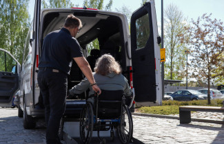 Asiakas on pyörätuolissa ja kuljettaja avustaa. Kuvaaja Anni Äikäs.