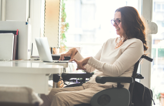 Nainen pyörätuolissa käyttää tietokonetta.