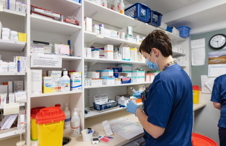 Sote-ammattilainen seisoo selin erilaisten lääkepurkkien edessä.