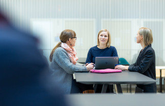 Kolme henkilöä istuvat pöydä ääressä.