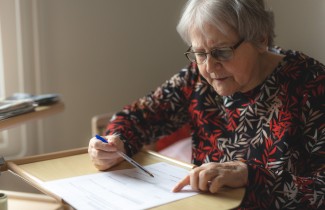 Iäkäs henkilö täyttää lomaketta.