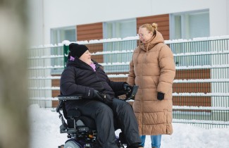 Henkilö pyörätuolissa ja hänen avustajansa.