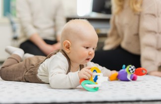 Vauva on mahallaan lattialla ja leikkii värillisillä leluilla.