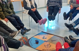 Ihmiset istuvat piirissä jalat ylhäällä, keskellä on pelilauta.