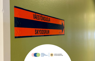 Väestönsuojan opastetarra rakennuksen seinällä