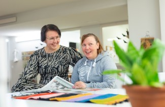 Asukas ja ohjaaja selaavat sanomalehteä pöydän ääressä