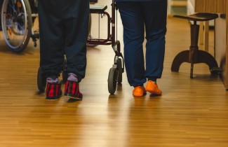 Ikäihminen rollaattorin kanssa kävelemässä hoitajan saattamana