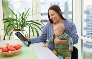 Aikuinen vauva sylissään. Katsovat tablet-tietokonetta.
