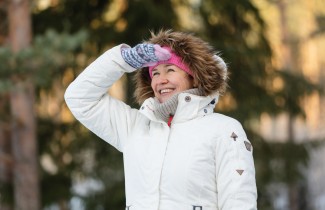 Nainen tähyilee iloisesti kaukaisuuteen talvivaatteissa.