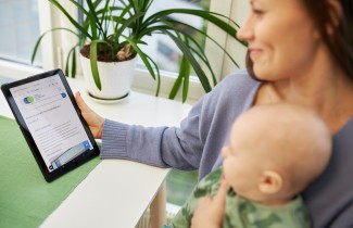 Nainen tablettitietokone kädessä ja vauva sylissä