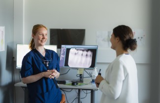 Kaksi suun terveydenhuollon ammattilaista keskustelevat hymyillen työpisteen ääressä.