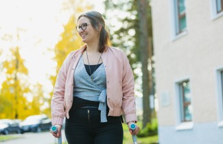 Hymyilevä nainen seisoo kyynärsauvojen kanssa parkkipaikalla aurinkoisessa syyssäässä