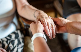 Hoitajan ja hoidettavan henkilön kädet.