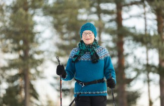 Iäkäs nainen sauvakävelee villapaita päällä ja taustalla on puita