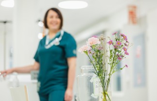 Hempeitä kukkia maljakossa henkilöstön taukotilassa, taustalla hoitaja työasussa.