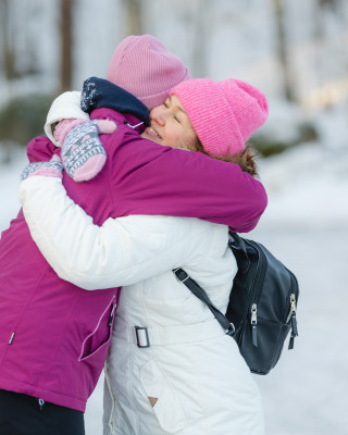Kaksi naista halaa toisiaan talvimaisemassa.