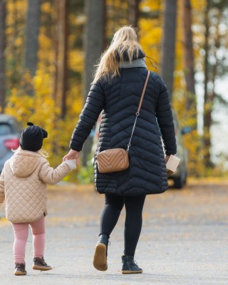 Äiti ja lapsi kävelemässä käsi kädessä parkkipaikalla.