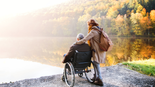 Henkilö istuu pyörätuolissa syysmaisemassa.