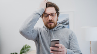 Ärsyyntynyt mies katsoo puhelinta ja lyö kättään päähänsä.