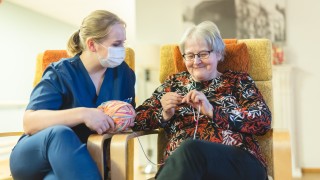 Sote-ammattilainen ja ikääntynyt henkilö neuloo.