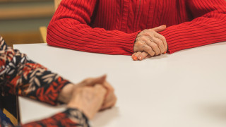 Kahden ikääntyneen henkilöt kädet lepäävät pöydällä.