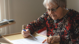 Ikääntynyt rouva täyttää lomaketta pöydän ääressä.
