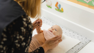 Vauva on hoitopöydällä ja katsoo terveydenhoitajaa.