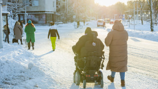 Pyörätuolia käyttävä henkilö ja avustaja kaupungissa.