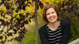 Nainen katsoo hymyillen kameraan puiden keskellä.