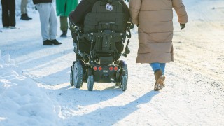 Pyörätuolia käyttävä henkilö ulkoilemassa kävelevän henkilön kanssa