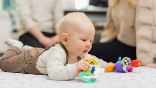 Vauva on mahallaan lattialla ja leikkii värillisillä leluilla.