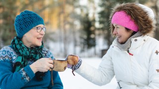 Kaksi iloista henkilöä kahvittelevat ulkona talvella.