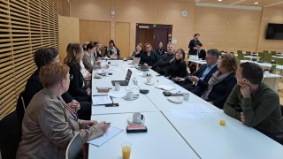 Ihmisiä istuu pitkän pöydän ääressä vastatusten.