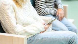 Kaksi nuorta istuu penkillä ja toisella on kännykkä kädessä.