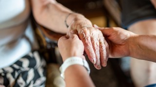 Hoitajan ja hoidettavan henkilön kädet.