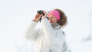 Nainen katsoo kiikareilla lumista maisemaa.