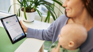 Nainen pitää vauvaa sylissä ja asioi verkkopalvelussa tabletilla