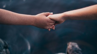 Kahden ihmiset kädet pitävät toisistaan kiinni järven yllä.