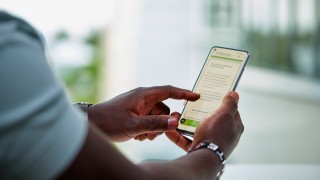 Ihminen pitää puhelinta kädessä ja selaa hyvinvointialueen Asioi verkossa -sivua.