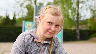 Tyttö katsoo kameraan ja taustalla näkyy leikkipuistoa