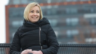 Nainen istumassa viileässä säässä penkillä iloisena.