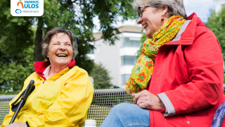 Kaksi iloista ikäihmistä istuu ulkona penkillä.  Vie vanhus ulos -kampanjan kuva.