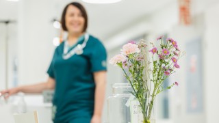Hempeitä kukkia maljakossa henkilöstön taukotilassa, taustalla hoitaja työasussa.